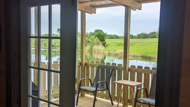Una terraza de madera con vista a un lago y campos cubiertos de hierba.