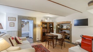 Een woonkamer met een bank, een eettafel en stoelen. Er is een boekenkast, een radiator en een televisie aan de muur.