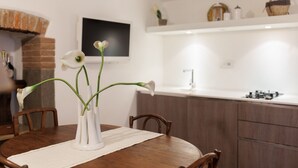 Een eettafel met een vaas witte bloemen, houten stoelen en een bakoven op de achtergrond.