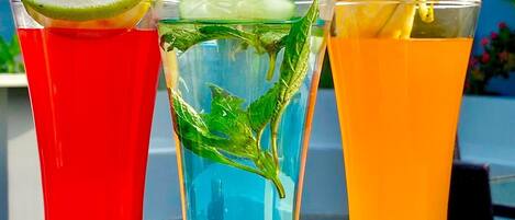 Tres vasos de bebidas con lima y menta, colocados al aire libre con vista a zonas verdes.