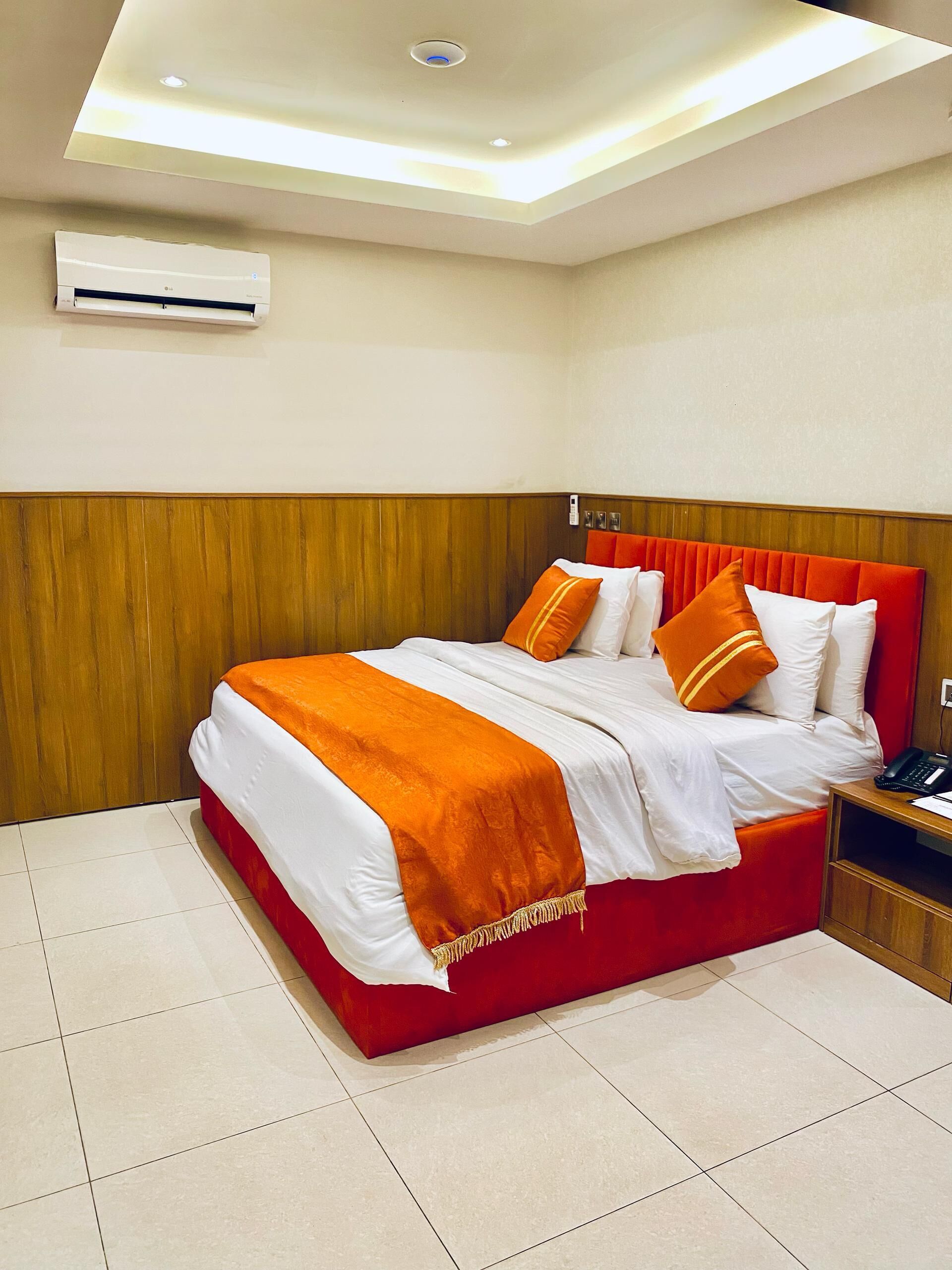 A hotel room with a large bed, a wooden headboard, a red accent wall, and a ceiling light fixture.