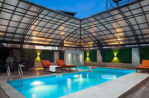 Une piscine intérieure dotée de chaises longues et d’une structure de plafond en verre.