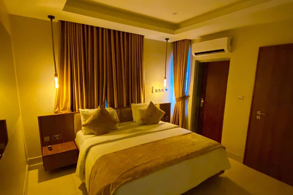 A modern bedroom with a large bed, a nightstand, an air conditioning unit, and a door.