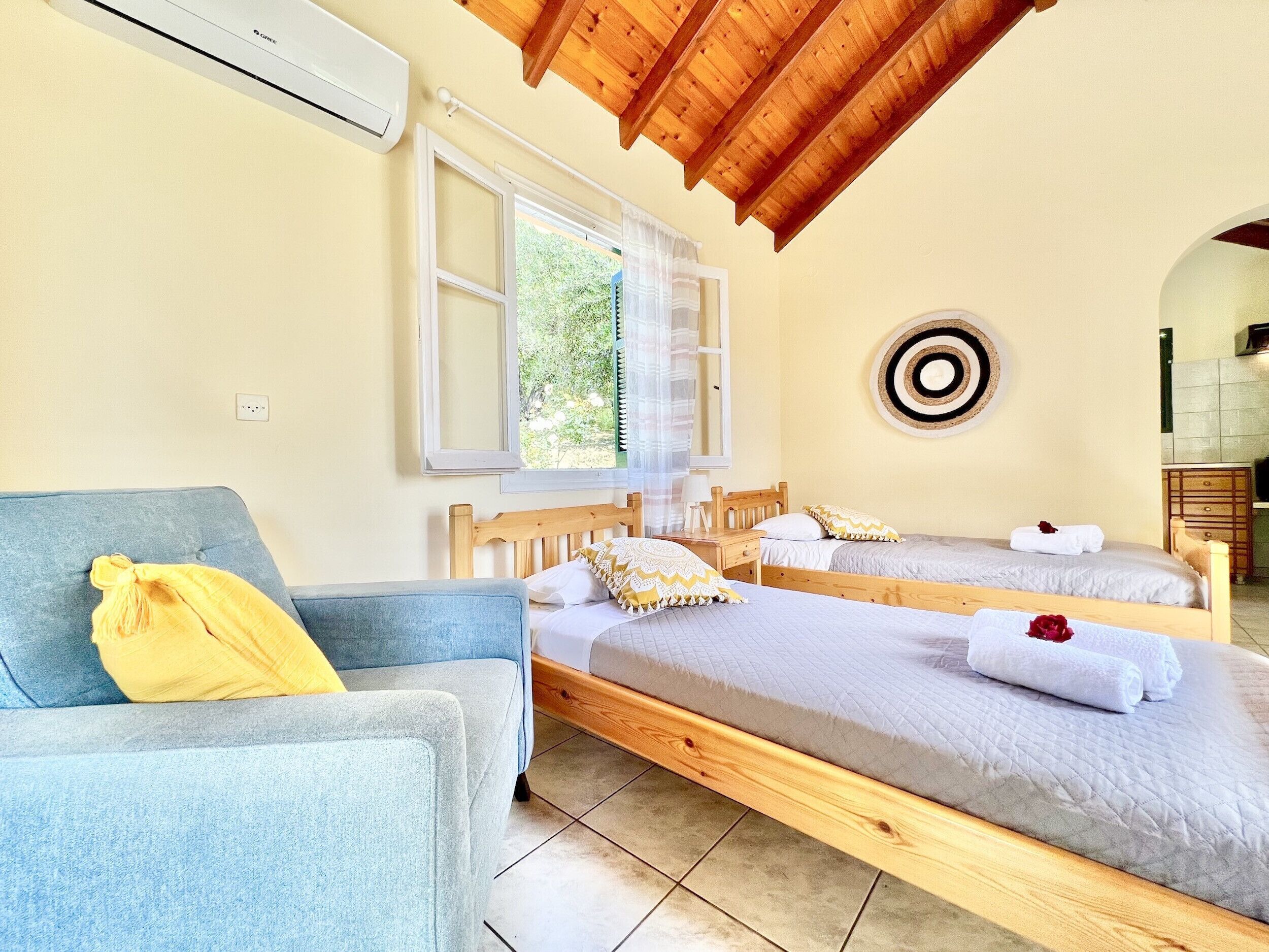 Una habitación con dos camas de madera, un sofá azul y una ventana con cortinas.