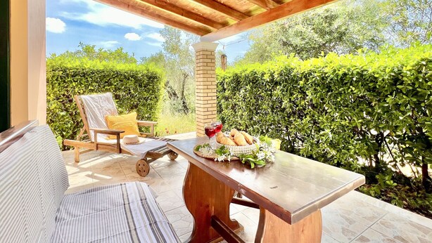 A covered patio with a wooden table, a cushioned chair, and a bench. - Renas Studio near Roda (Roda)