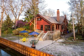 A red cabin with a wooden deck, outdoor seating, and a dock.