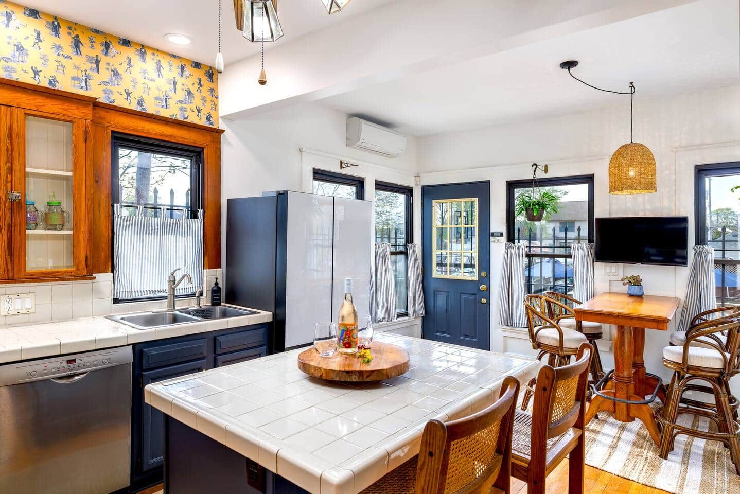 A modern kitchen with a central island, built-in appliances, and a dining area with wicker chairs.