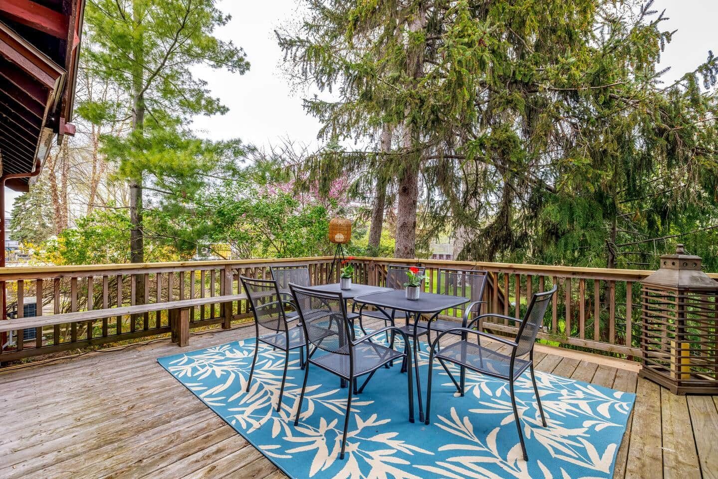 A wooden deck with a table and chairs, surrounded by trees and a railing.
