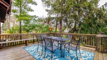 A wooden deck with a table and chairs, surrounded by trees and a railing.