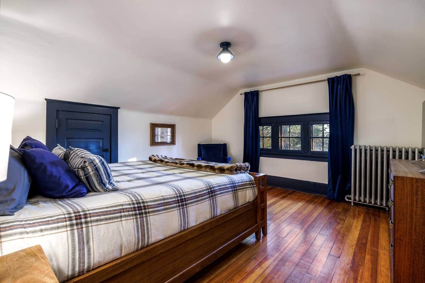 A bedroom with a wooden bed, a radiator, a window with curtains, and a ceiling light.