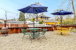 An outdoor patio area with a table and chairs, two umbrellas, and a barbecue grill.