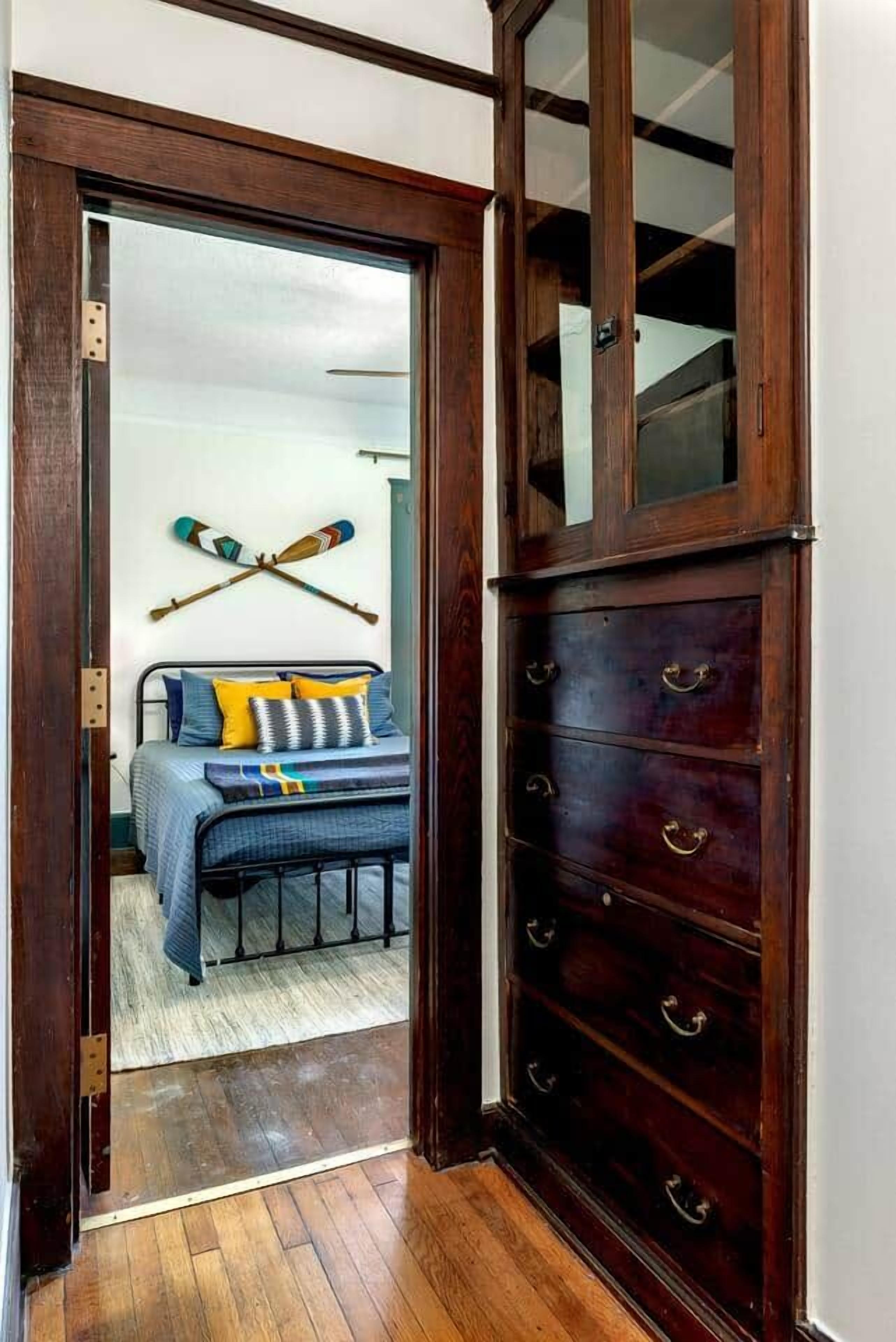 A bedroom with a bed, a wooden dresser, and a door leading to another room.