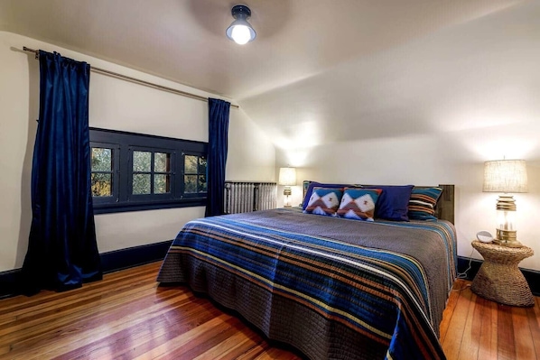 Une chambre à coucher avec un grand lit, des rideaux foncés, une fenêtre, deux lampes de chevet et un luminaire au plafond.