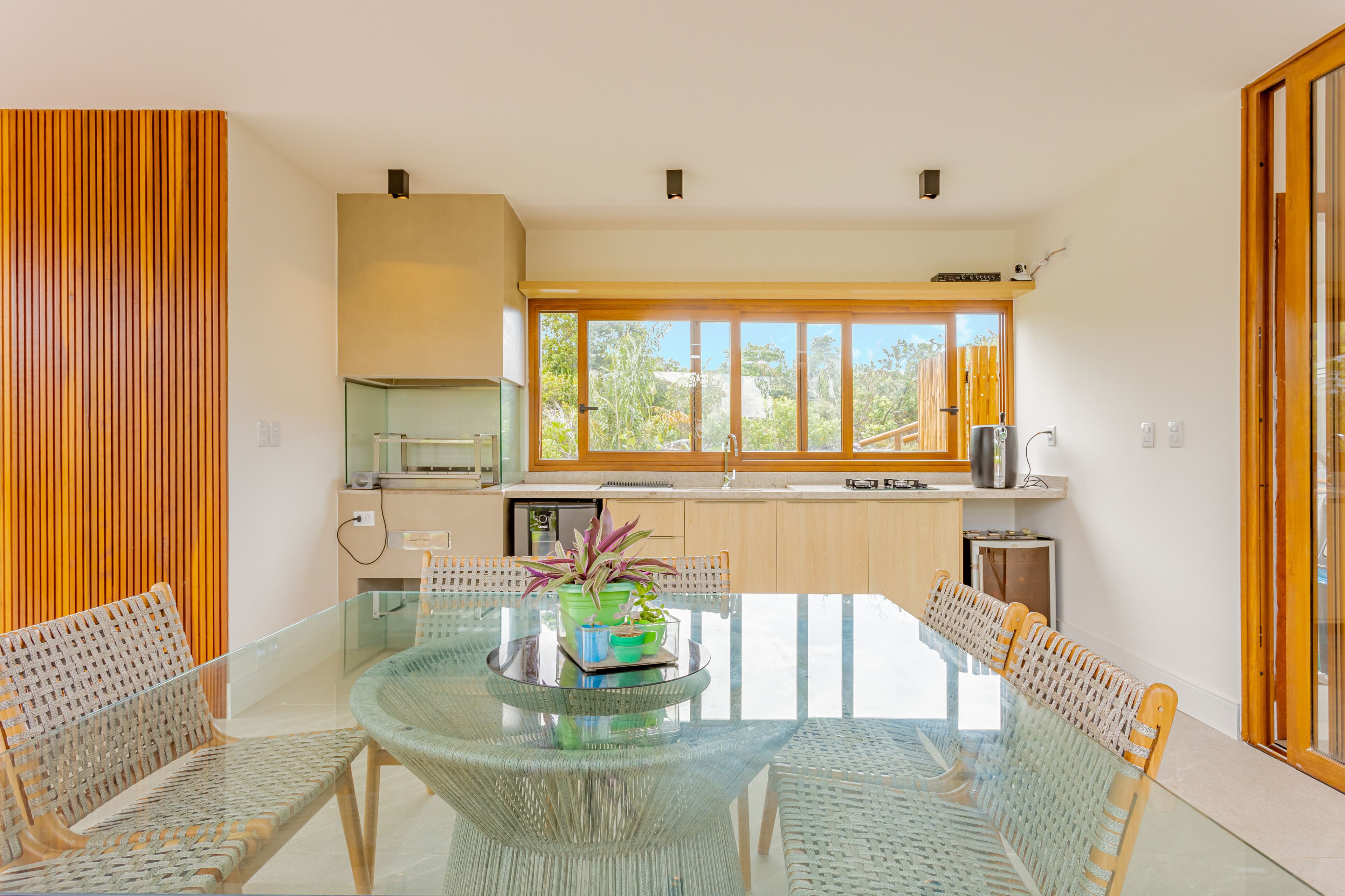 Een moderne keuken met een groot raam, een eethoek met een glazen tafel, en houten details.