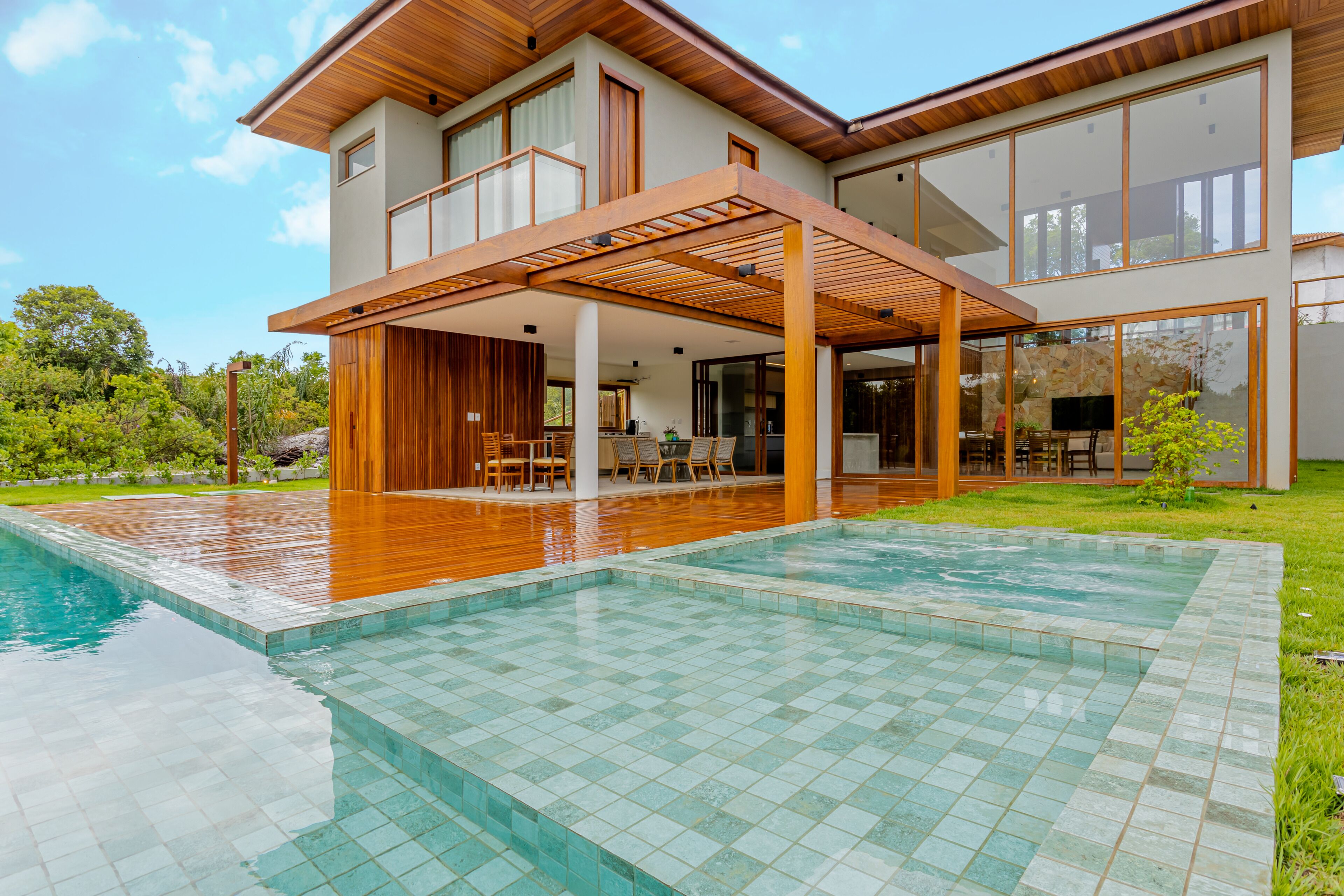 Une maison moderne dotée d’une grande piscine, d’une terrasse en bois et d’un espace extérieur couvert.