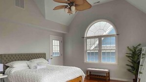 Un dormitorio con una cama grande, un ventilador de techo, una ventana con vistas y suelo de madera.
