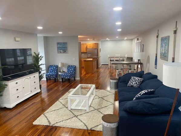A modern living room with a flat-screen TV, a sofa, a coffee table, and patterned chairs. - Welcome to Ocean’s 55 ! (Milford)