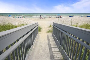 A beach pathway leading to the shore with beach umbrellas and people.