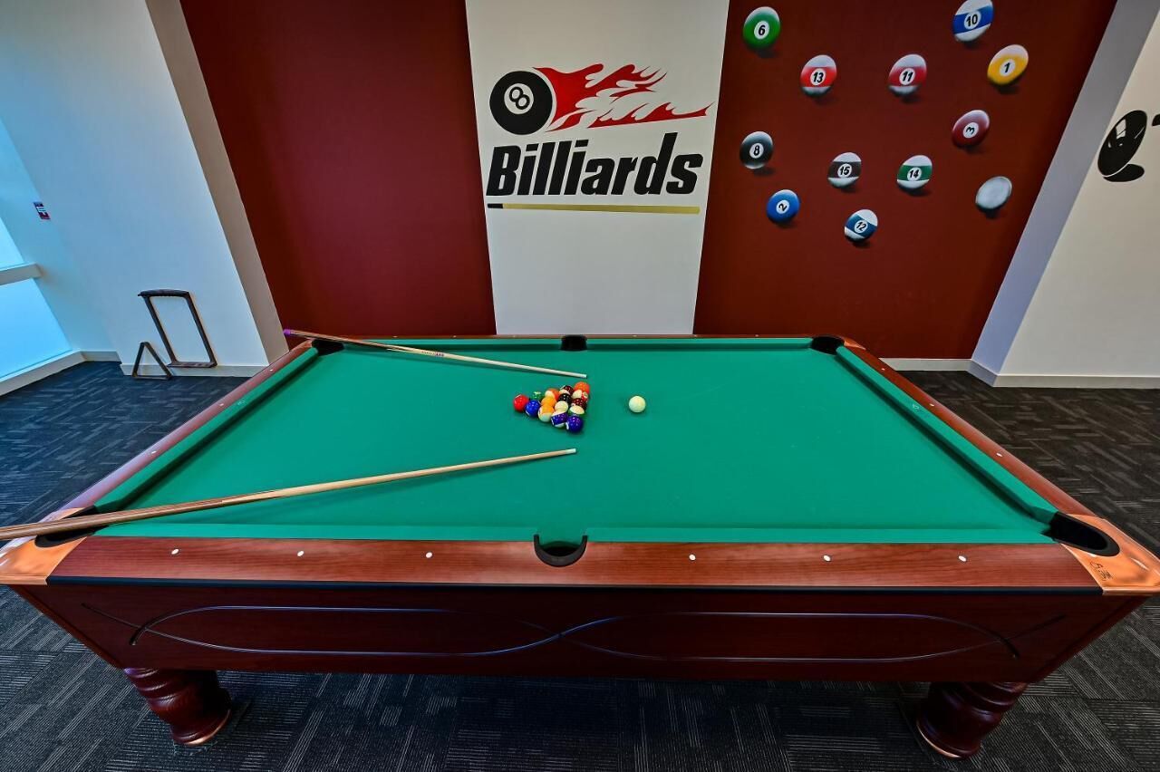 Ett biljardbord med bollar och köer, en biljardlogotyp och en vägg med numrerade bollar.
