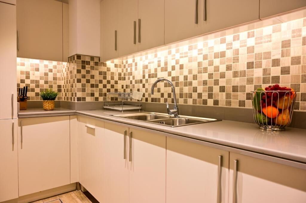 A modern kitchen with a checkered backsplash, stainless steel sink, and a fruit bowl on the counter.