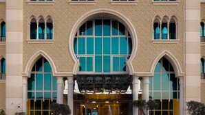 Un hotel de varios pisos con una entrada arqueada central, grandes ventanales y una fuente en el patio.
