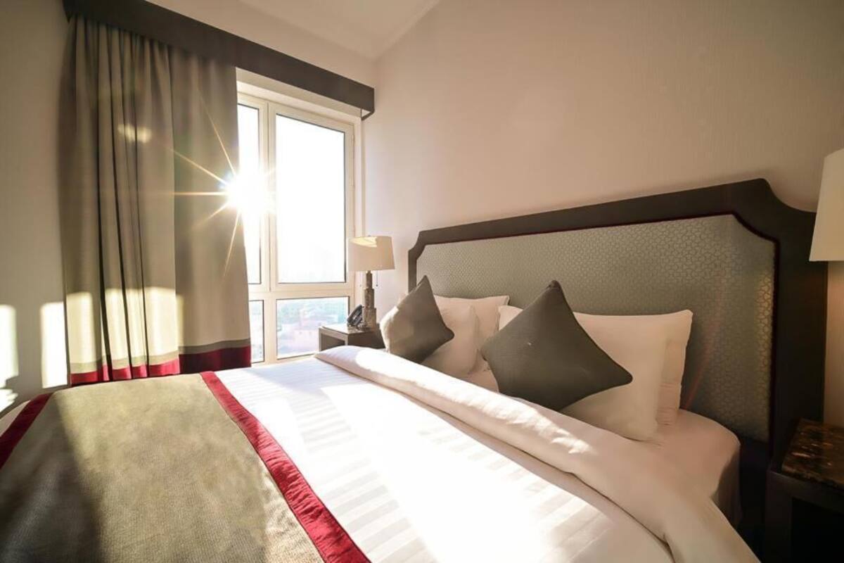 Habitación de hotel con una cama grande, una ventana con cortinas, una mesita de noche con lámpara y vistas al exterior.