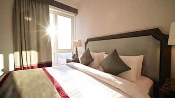 A hotel room with a large bed, a window with curtains, a nightstand with a lamp, and a view of the outdoors.