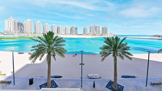 Una playa con palmeras y un horizonte urbano al fondo.