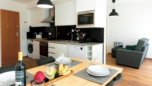 Eine moderne Küche mit Mikrowelle, Backofen und Geschirrspüler. Ein Essbereich mit Tisch für zwei Personen und ein graues Sofa im Wohnbereich.