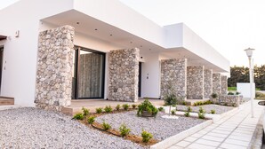 A modern building with a stone facade, large windows, and a well-maintained garden. - Pebble Garden (Kos)