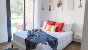 A bedroom with a bed, a nightstand, a window, and artwork on the wall. - Pebble Garden (Kos)