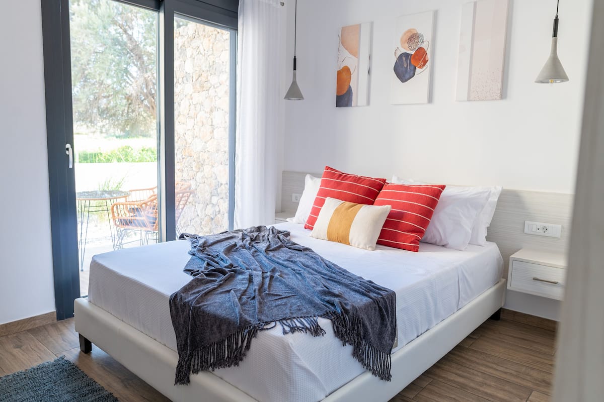 Un dormitorio con cama, mesita de noche, ventana y una obra de arte en la pared.