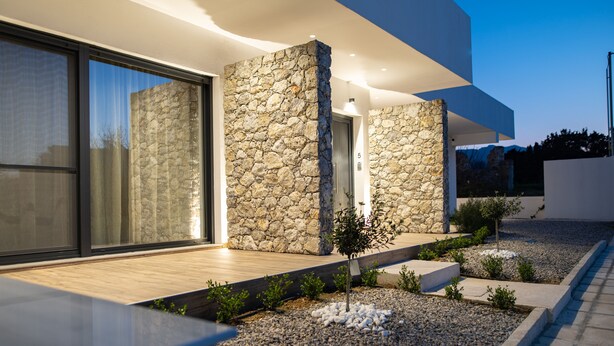 A modern building with stone walls, a wooden deck, and a gravel garden. - Pebble Garden (Kos)