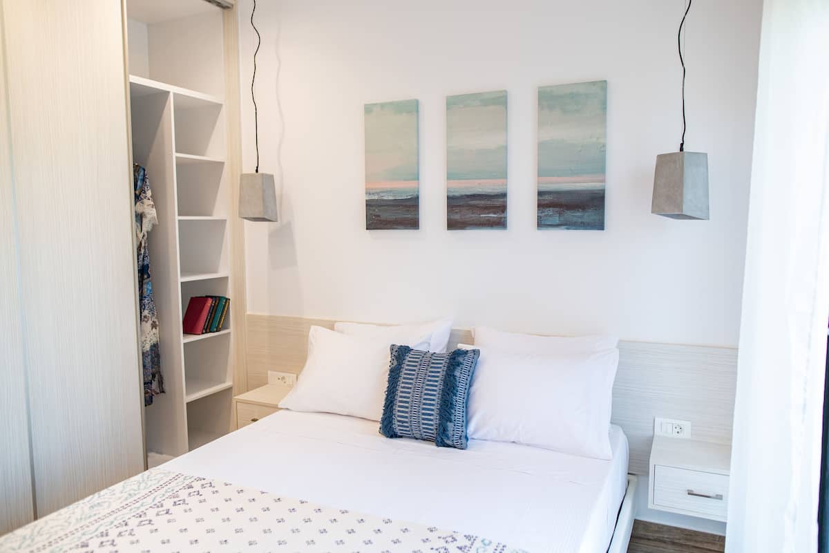 Un dormitorio ordenado con cama, mesitas de noche, armario y una obra de arte en la pared.