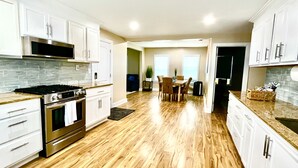 Una cocina moderna con armarios blancos, una estufa de acero inoxidable y un comedor con mesa y sillas.