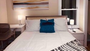 Una habitación de hotel con una cama, dos mesitas de noche, una silla, una ventana y un cuadro en la pared.