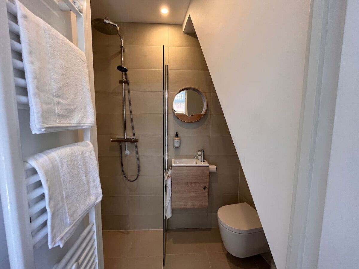 A modern bathroom with a glass-enclosed shower, a round mirror, a wooden vanity, and a white toilet.