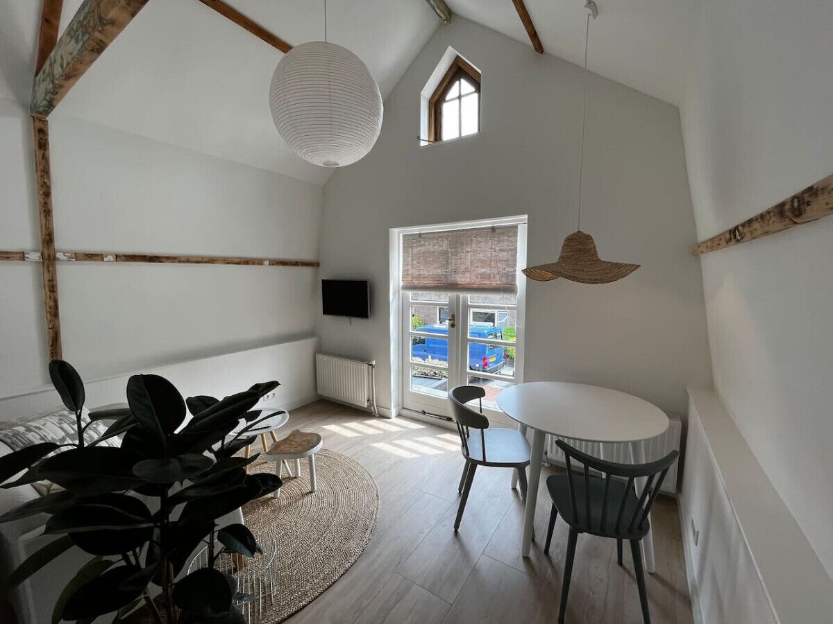 Una stanza con soffitto alto, travi a vista in legno, un tavolo rotondo con sedie, un'ampia finestra vista esterna e un lampadario.