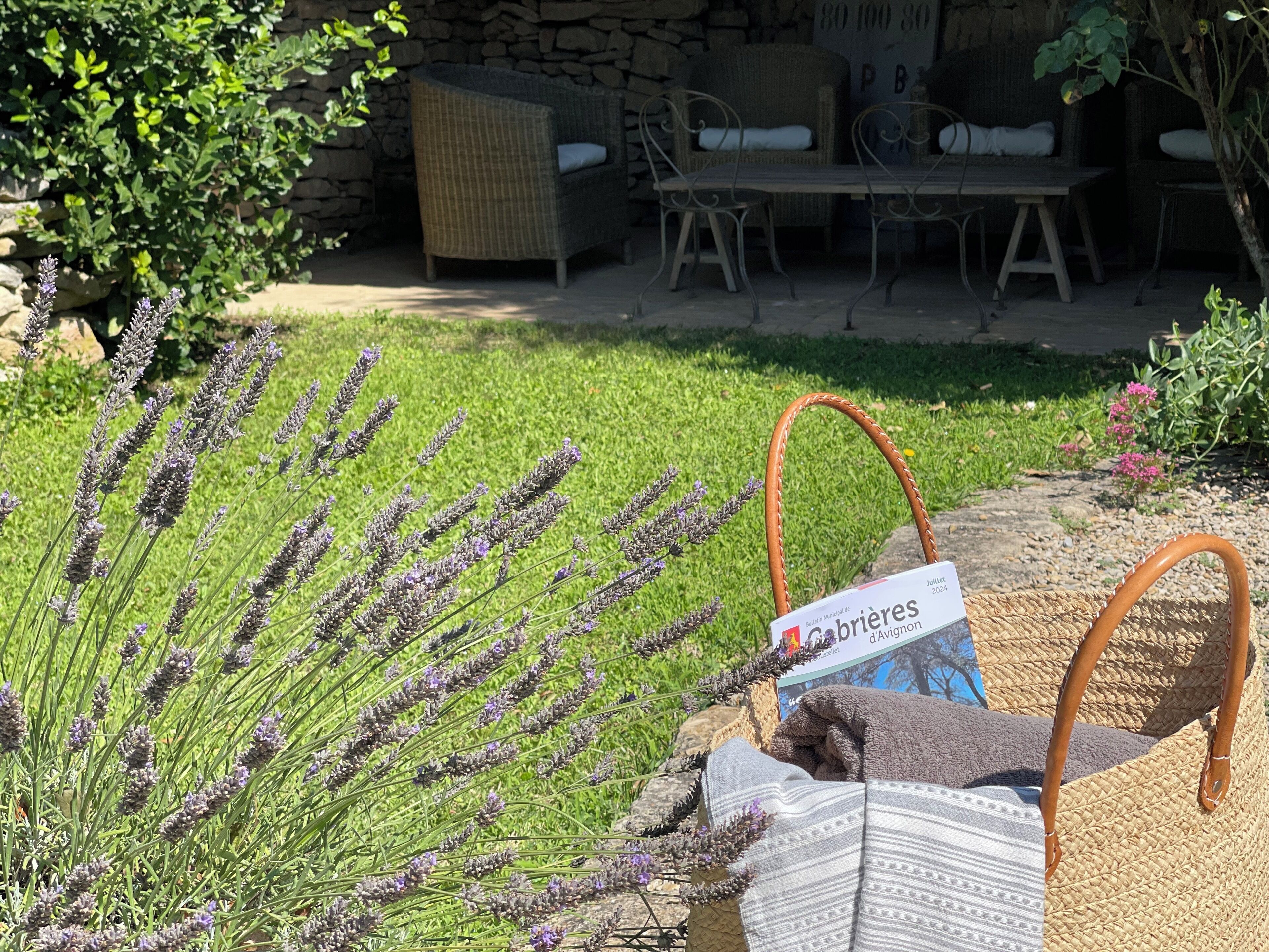A garden with lavender plants, a wicker chair, and a table with a sign indicating an event.
