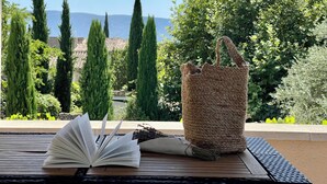 An open book on a wooden table with a woven bag and a bouquet of flowers.