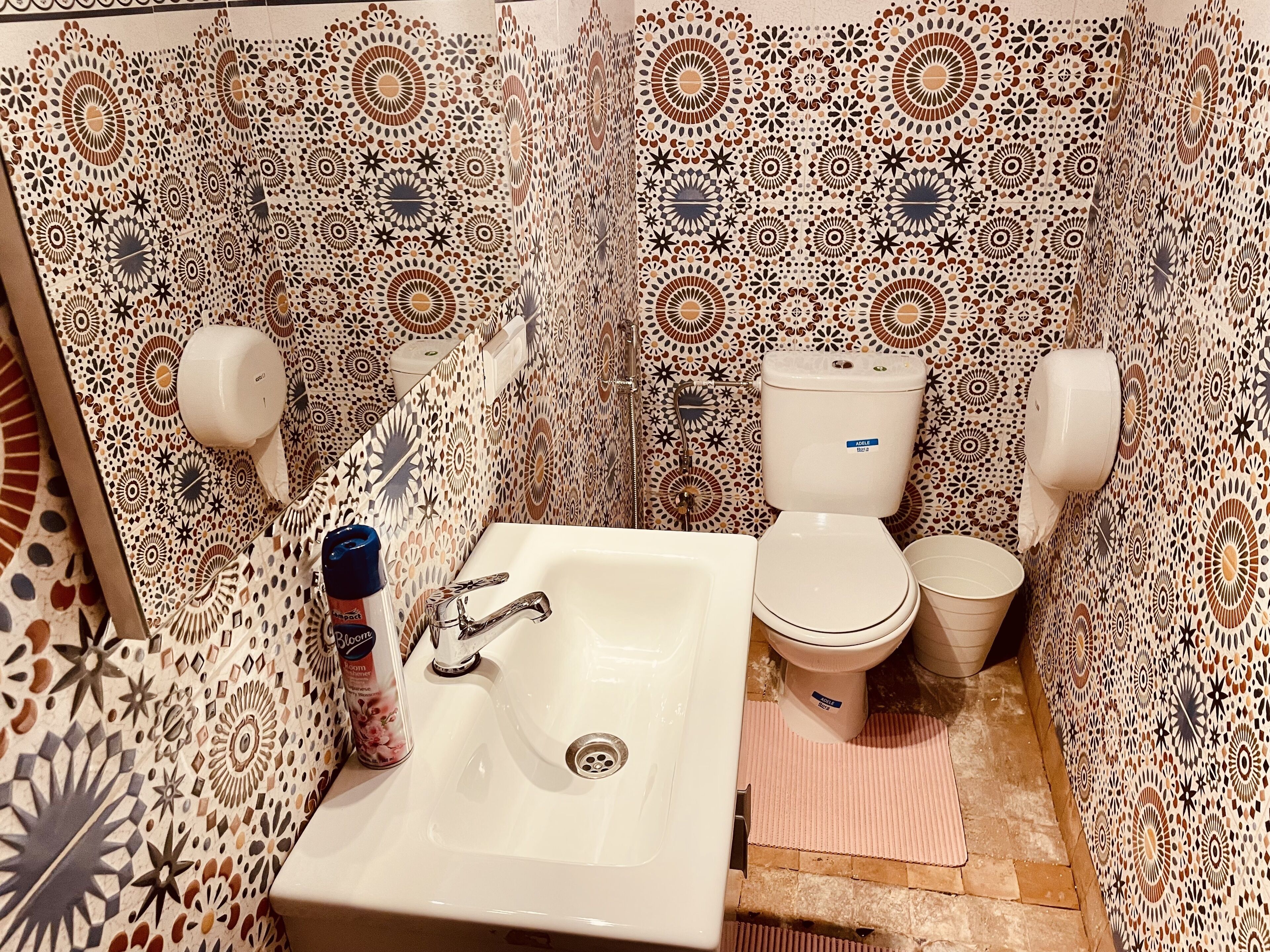 A bathroom with patterned tiles, a sink, a toilet, and a hand dryer.