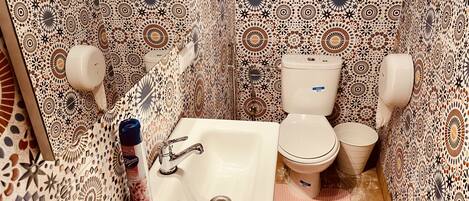 Une salle de bain avec des carreaux décorés, un lavabo, des toilettes et un sèche-mains.