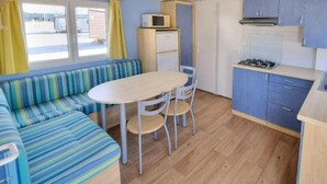 A compact kitchenette with a stove, microwave, and cabinets. There is a striped sofa and a small round table with chairs. - Mobile Home 6 Domaine DE LA Grange DES Champs (Lorris)