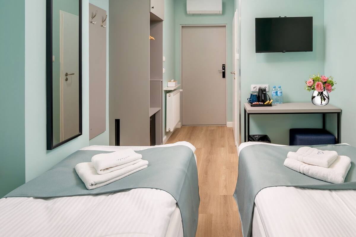 A hotel room with two beds, a TV, a desk with a vase of flowers, and a view of the hallway.