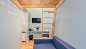 A compact room with a wooden ceiling, a blue sofa, a small desk with a TV, and a plant. - Hostel JessApart - Aleje Jerozolimskie (Warsaw)