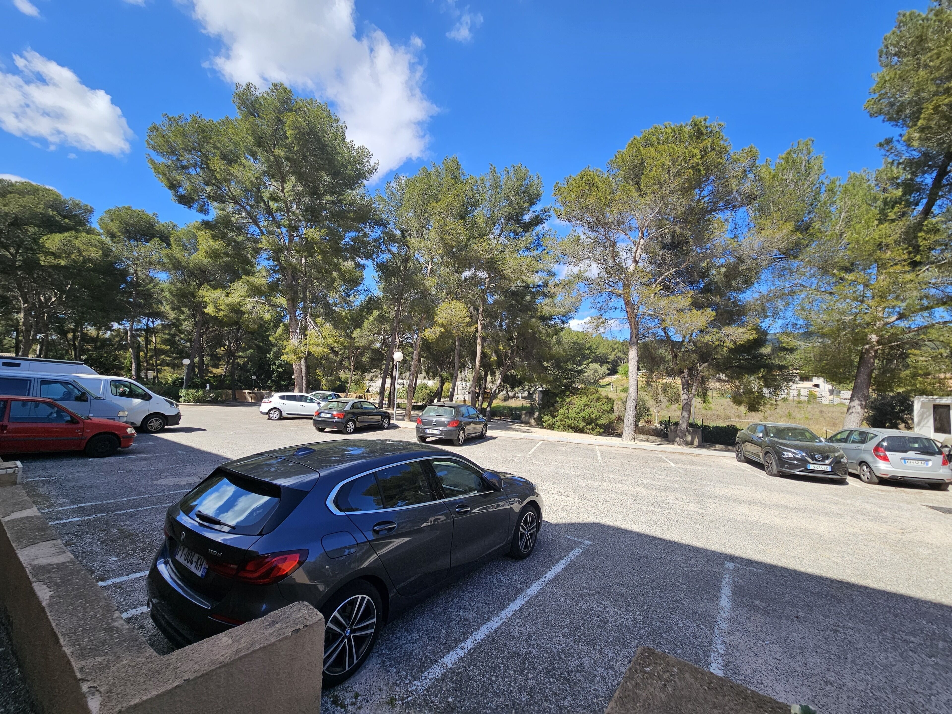A parking lot with several cars, surrounded by trees and a clear blue sky.