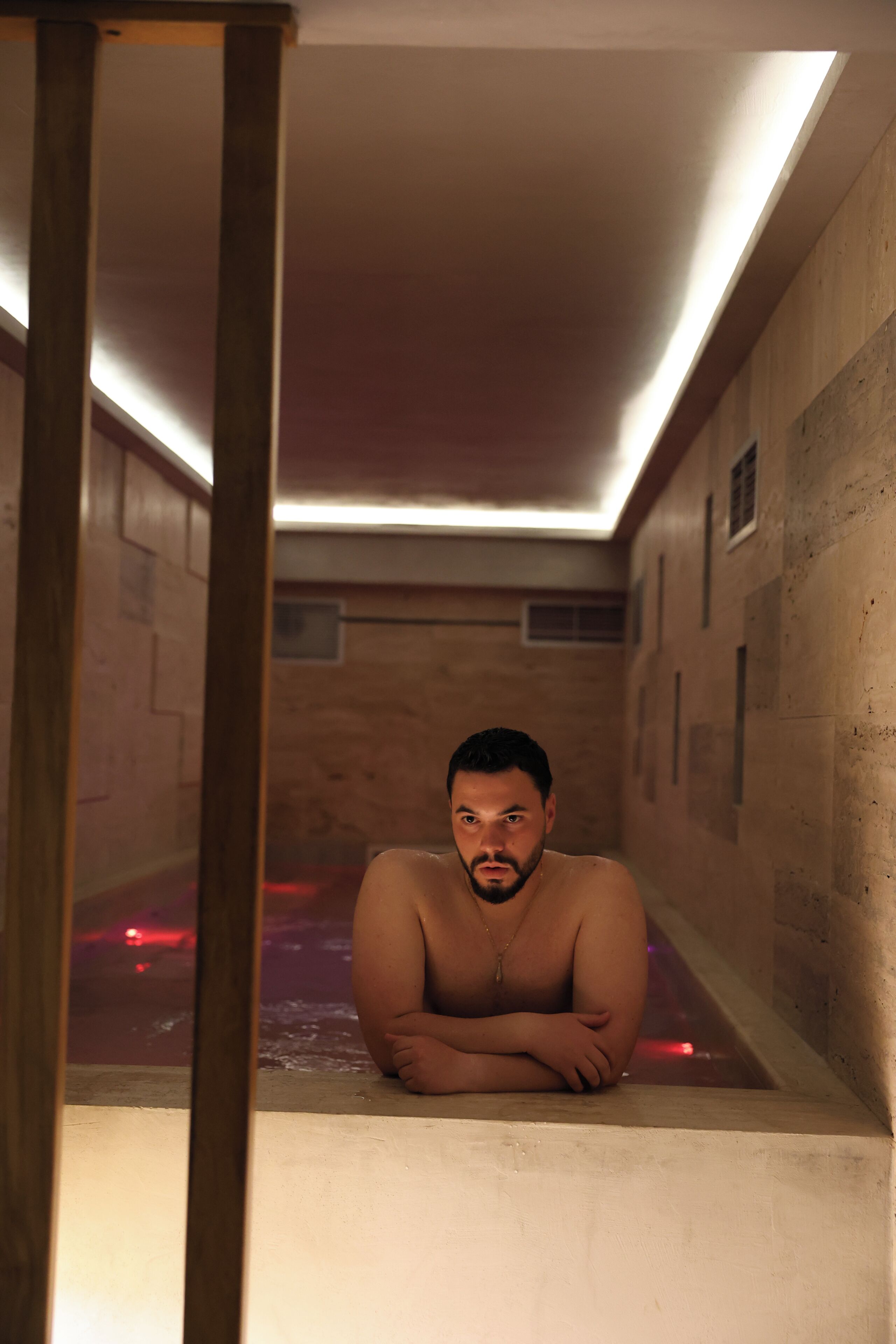 A man in a bathtub with wooden walls and a ceiling light.
