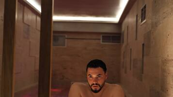 A man in a bathtub with wooden walls and a ceiling light.