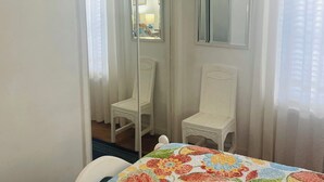 Habitació d'hotel amb un llit, una televisió penjada a la paret, una cadira, un mirall i una porta que dóna a una altra habitació.