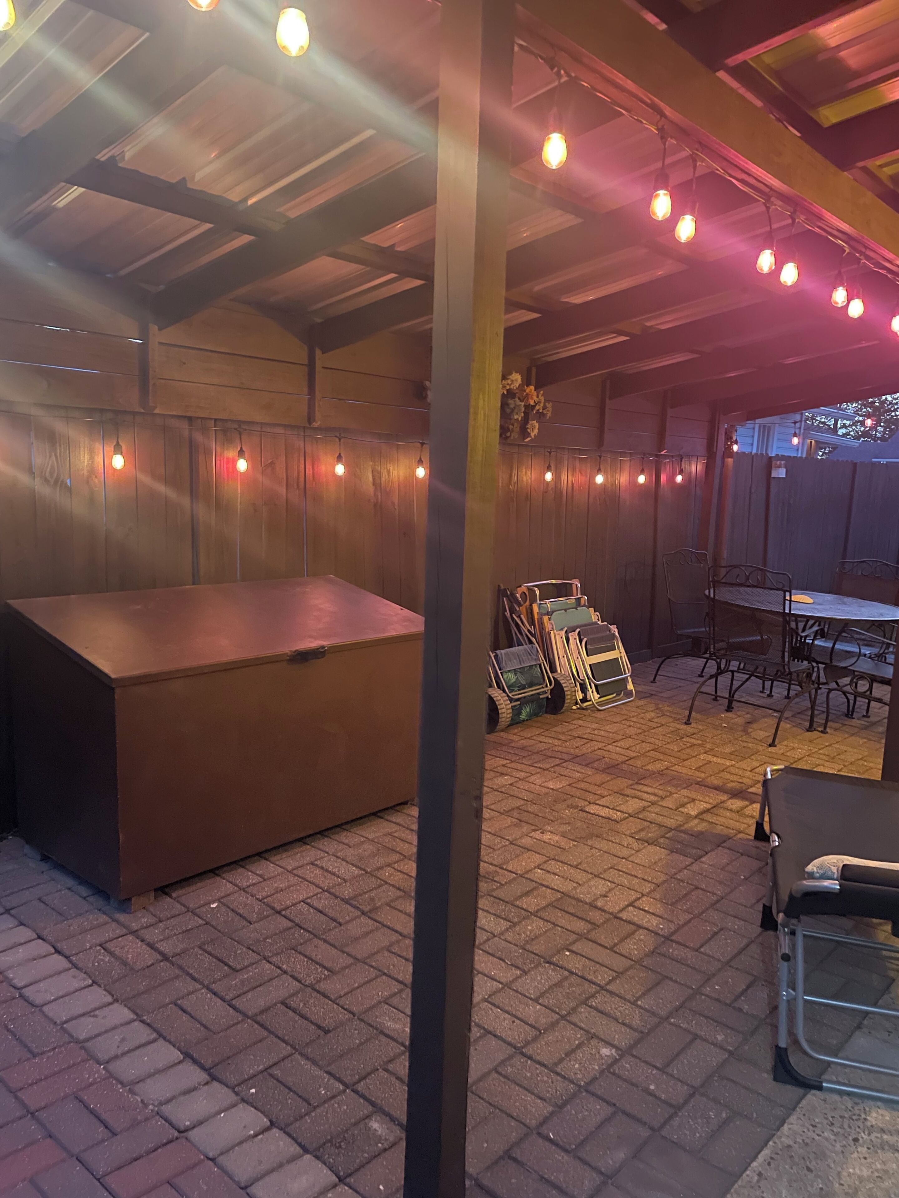Un espace extérieur aménagé en terrasse, avec une longue table et des chaises, une clôture en bois et un sol en briques.